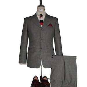 May include: A gray three-piece suit displayed on a mannequin, including a blazer, trousers, and a vest. The blazer features a pocket square and is paired with a striped tie. Brown leather tassel loafers complete the ensemble.
