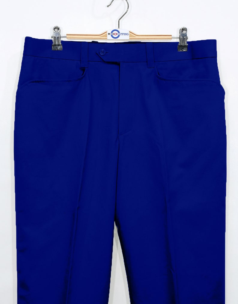 May include: A pair of blue pants hanging on a wooden hanger. The pants have a button closure and two front pockets.