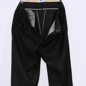 May include: Black dress pants with a zipper fly and button closure. The pants are hanging on a wooden hanger with a tag that says "MOD'S PRING".