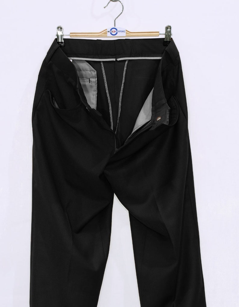 May include: Black dress pants with a zipper fly and button closure. The pants are hanging on a wooden hanger with a tag that says "MOD'S PRING".