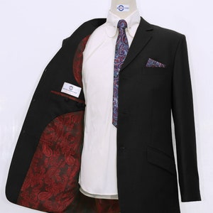 May include: A black suit jacket with a paisley patterned lining. The jacket has a single button closure and a pocket on the left breast. The jacket is on a mannequin wearing a white shirt and a blue paisley tie.