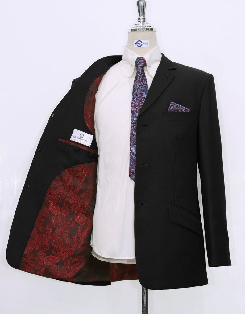 May include: A black suit jacket with a paisley patterned lining. The jacket has a single button closure and a pocket on the left breast. The jacket is on a mannequin wearing a white shirt and a blue paisley tie.