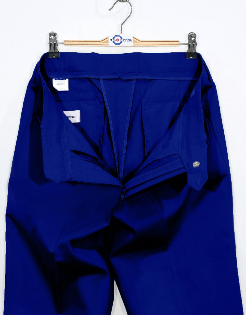 May include: A pair of blue pants with a zipper and button closure. The pants are folded in half and hanging on a wooden hanger.