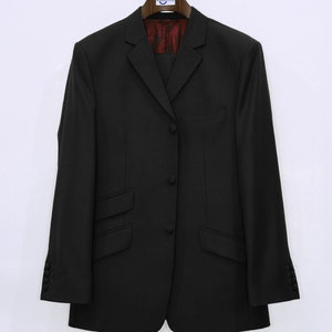 May include: A black blazer with a single button closure and two flap pockets. The blazer has a plain design and is hanging on a wooden hanger.