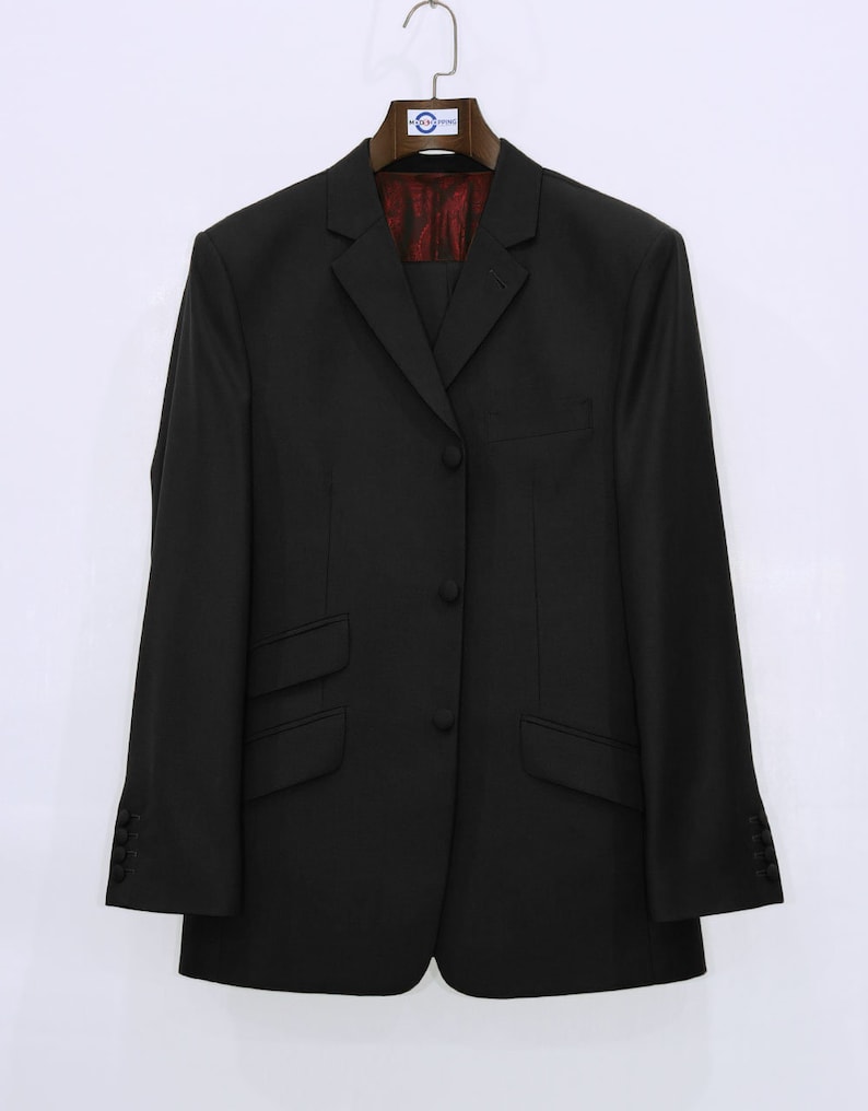 May include: A black blazer with a single button closure and two flap pockets. The blazer has a plain design and is hanging on a wooden hanger.