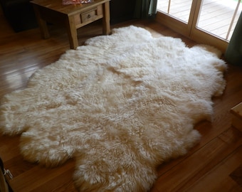 May include: A large, fluffy white sheepskin rug. The rug is laid out on a wooden floor.