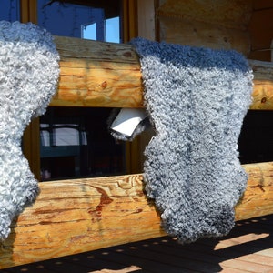 Op de afbeelding: Drie grijze schapenvachten hangen aan een houten leuning. De vachten zijn pluche en hebben een natuurlijke, rustieke uitstraling.