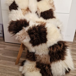 Könnte beinhalten: Ein Schaffellteppich mit Patchwork-Muster in Weiß- und Brauntönen. Der Teppich besteht aus weichem, flauschigem Fell und ist perfekt, um jedem Raum eine warme und gemütliche Atmosphäre zu verleihen.