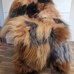 May include: A sheepskin rug with a mix of brown, black, and gray fur. The rug is fluffy and soft, and it would be perfect for adding a touch of warmth and comfort to any room.