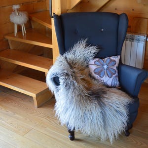May include: A dark blue armchair with a fluffy, light-colored throw and a floral pillow. A decorative sheep figurine sits on a wooden staircase in the background. The room has wooden walls and flooring.