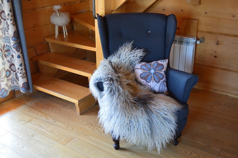 May include: A dark blue armchair with a fluffy, light-colored throw and a floral pillow. A decorative sheep figurine sits on a wooden staircase in the background. The room has wooden walls and flooring.