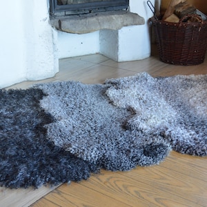 Op de afbeelding: Een pluche schapenvachtkleed met een verloop van grijs en zwart. Het kleed ligt op een houten vloer.