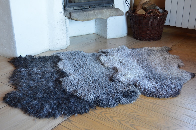 Op de afbeelding: Een pluche schapenvachtkleed met een verloop van grijs en zwart. Het kleed ligt op een houten vloer.