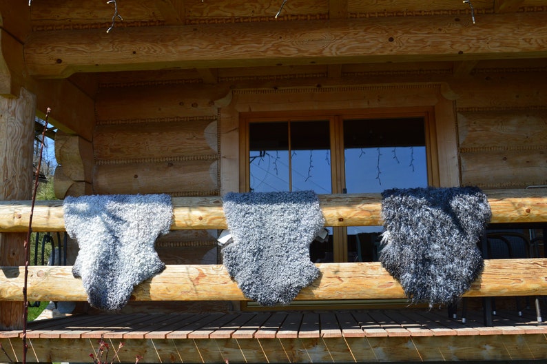 Op de afbeelding: Drie grijze schapenvachten hangen aan een houten leuning buiten een blokhut. De vachten hangen aan een houten leuning buiten een blokhut.