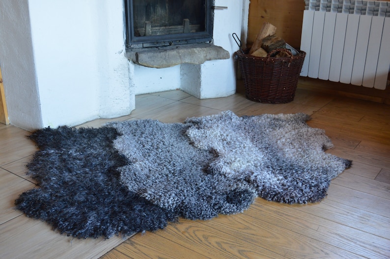 Op de afbeelding: Een grijs en zwart shagtapijt met een verloopdessin. Het tapijt is gemaakt van lange, pluche vezels en heeft een natuurlijke, rustieke uitstraling.