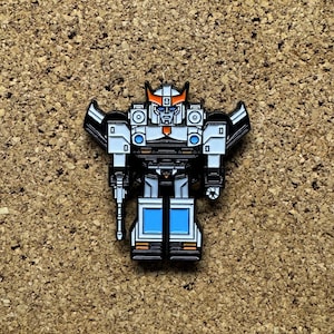 May include: A white and black enamel pin of a robot with a blue and white chest, orange and white helmet, and a gun in its right hand.