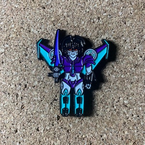 May include: Purple and teal robot pin with wings and a sword. The robot has a black helmet and white eyes.