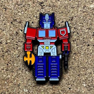 May include: A red, blue, and yellow robot pin with a sword. The robot is holding a sword in its right hand and has a shield on its left arm.