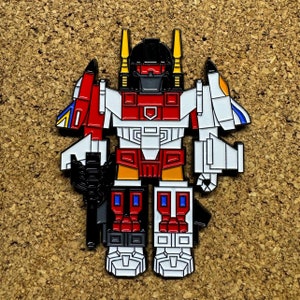 May include: A red, white, and black robot pin with yellow accents. The robot has a large head with a black visor and a red chest plate. The robot is holding a gun in its right hand and a sword in its left hand.