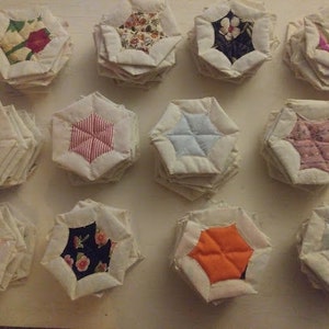 May include: A collection of 12 handmade fabric hexagons, each with a different floral pattern. The hexagons are layered and sewn together to create a unique and decorative piece.
