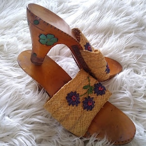 Könnte beinhalten: Ein Paar braune Holzplattformsandalen mit einem gewebten Strohoberteil und Blumenstickerei. Die Sandalen haben einen hohen Absatz und eine dicke Plattform.
