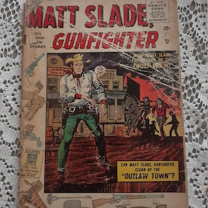 Op de afbeelding: Een vintage comicboekomslag met een cowboy-personage genaamd Matt Slade, de revolverheld. De omslagillustratie toont Matt Slade staand in een westelijke stad, met een pistool in zijn hand en een vastberaden uitdrukking op zijn gezicht. De tekst op de omslag luidt "Matt Slade, Gunfighter" en "Kan Matt Slade, de revolverheld, de "Outlaw Town" opruimen?"