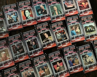 May include: A collection of VHS tapes featuring episodes of the original Star Trek television series. The tapes are arranged in a grid pattern and feature various characters from the show, including Captain Kirk, Spock, and Dr. McCoy.