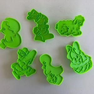 Puede incluir: Conjunto de seis cortadores de galletas de plástico verde con forma de pollito, conejito, cordero, pato, niña con sombrero y niña con vestido.