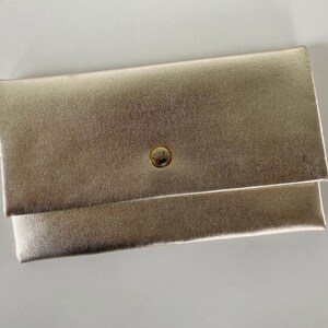 May include: A gold clutch bag with a single button fastening.