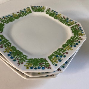 May include: A set of three white octagonal plates with a green, yellow and blue floral pattern around the edge.