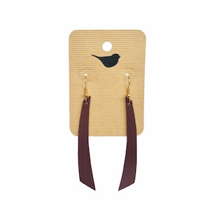 May include: A pair of long, burgundy leather earrings with gold hooks. The earrings are hanging from a brown card with a small bird silhouette.