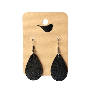 May include: A pair of black leather teardrop earrings with silver hooks. The earrings are displayed on a brown card with a small bird silhouette.