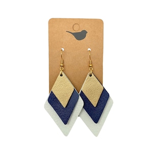 May include: A pair of gold, navy blue, and white leather earrings with a diamond shape. The earrings are hanging from gold hooks.