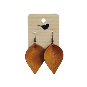 May include: A pair of brown leather teardrop earrings with gold hooks. The earrings are displayed on a brown card with a small bird silhouette.