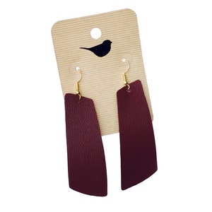 May include: A pair of burgundy leather earrings with gold hooks. The earrings are rectangular in shape and have a slightly curved edge.