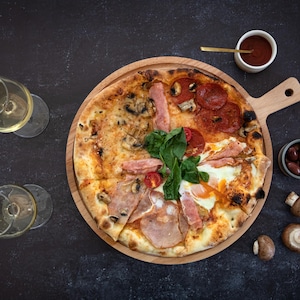 K&ouml;nnte beinhalten: Eine Pizza, unterteilt in Abschnitte mit verschiedenen Bel&auml;gen, darunter Peperoni, Schinken und Pilze, auf einem Holzbrett. Serviert mit Weingl&auml;sern, Oliven, Pilzen und einer kleinen Sch&uuml;ssel mit Sauce. Die Pizza wird auf einer dunklen Oberfl&auml;che pr&auml;sentiert.