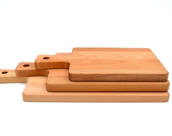 May include: Three wooden chopping boards stacked on top of each other. The top board has a handle and is the largest. The bottom board is the smallest.