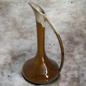 May include: A brown ceramic pitcher with a white glaze on the top and handle. The pitcher has a wide base and a narrow neck.