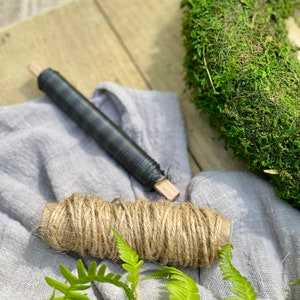 May include: A roll of natural twine, a roll of black wire, and a green moss wreath on a light gray fabric surface.