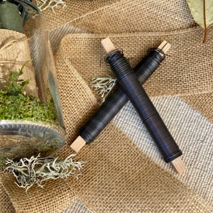 May include: Two spools of black wire wrapped around wooden dowels. The spools are lying on a brown hessian surface.