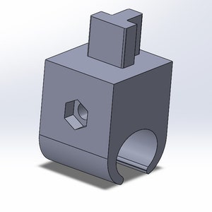 May include: A gray, 3D-rendered mechanical component. It features a T-shaped projection on top of a cube-shaped body. The body has a hexagonal opening and a curved, ring-like base. The component is designed with a slot.