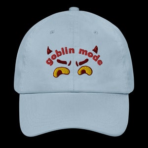 May include: A light blue baseball cap with red embroidered text that says "goblin mode" with a pair of red devil horns and yellow eyes.