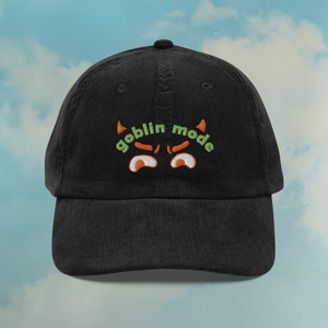 May include: Black corduroy baseball cap with green and orange embroidery that reads "goblin mode".