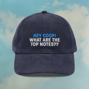 May include: Navy blue corduroy baseball cap with the text "HEY COOP! WHAT ARE THE TOP NOTES??" embroidered in white and blue. The cap has a curved peak and a button on top.