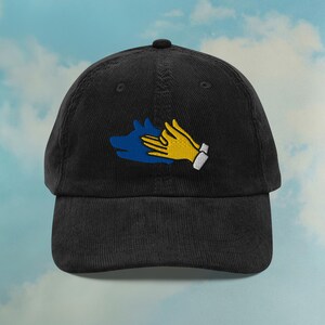 May include: Black corduroy baseball cap with an embroidered design of a blue hand and a yellow hand shaking.