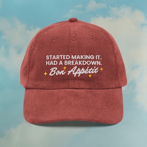 Puede incluir: Gorra de béisbol de pana burdeos con la frase bordada "STARTED MAKING IT. HAD A BREAKDOWN. Bon Appétit" en blanco, con detalles de estrellas amarillas. La gorra tiene una visera curva y una parte superior redonda.