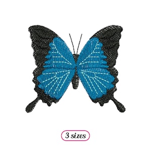 Puede incluir: Diseño bordado de una mariposa azul con alas negras. La mariposa está centrada en un fondo blanco. El texto "3 tamaños" está debajo de la mariposa.