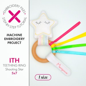 以下が含まれることがあります： 白い流れ星と虹色のリボンが付いた歯固めリングの機械刺繍プロジェクト。リングは木でできており、星は顔の刺繍が施されています。テキスト「ITH Teething Ring Shooting Star 5x7 1 size Margaux」が表示されています。