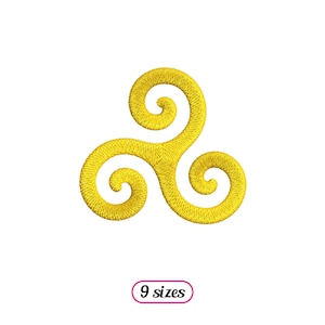 Puede incluir: Un diseño bordado amarillo de un triskelion, un símbolo de tres espirales entrelazadas. El diseño está sobre un fondo blanco.