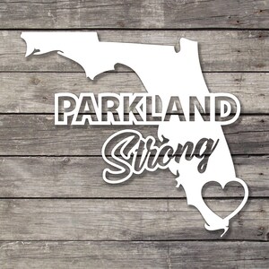 May include: White silhouette of the state of Florida with the words "Parkland Strong" and a heart in the centre. The background is a wood grain texture.
